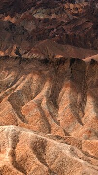 Vertical Screen: Death Valley National Park Zabriskie Point California showcases dramatic eroded mudstone badlands with golden brown ridges and deep shadows creating stunning desert landscape.