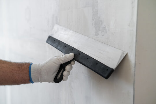 A professional is smoothing joint compound on a drywall surface using a hand trowel. The workspace features well prepared plasterboard and clean edges visible in the background.