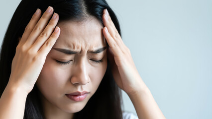 Naklejka premium A Woman Experiencing a Headache: A young Asian woman clutches her temples, her face contorted in pain, illustrating the discomfort and distress of a severe headache.