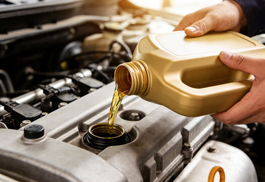 A close-up shot of a person's hands pouring fresh golden engine oil from a bottle into a car engine, highlighting routine vehicle maintenance.
