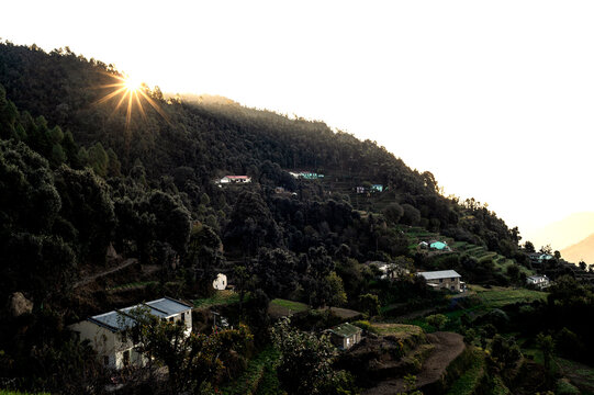 Golden Morning Sunburst Cresting Over Forested Slopes and Mountain Houses in Kanarkha Village, Kumaon, Uttarakhand, India.