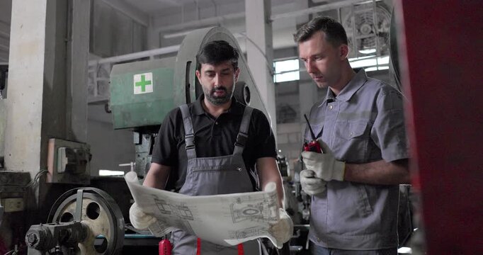 Factory Technicians Reviewing Blueprint During Machine Inspection in Metal Workshop