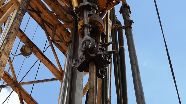 Drilling rig with top drive system (TDS) during tripping in the drill pipe to drill the hole in crude oil exploration operation with sunny blue sky background. Heavy industrial working scene.
