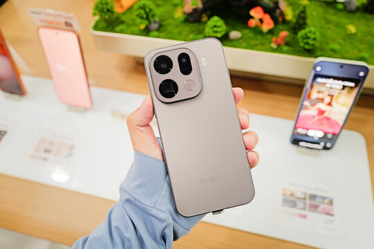 A close-up view of a person holding the OPPO Find X9 smartphone in a sleek silver-grey color on display at a retail store.