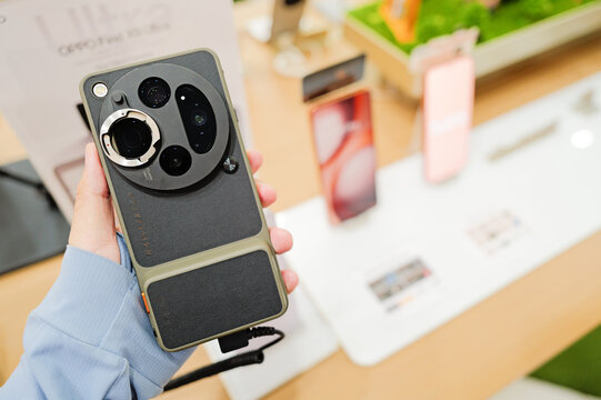 A close-up view of a person holding the OPPO Find X9 Ultra smartphone equipped with a specialized photography camera case and lens adapter on display.