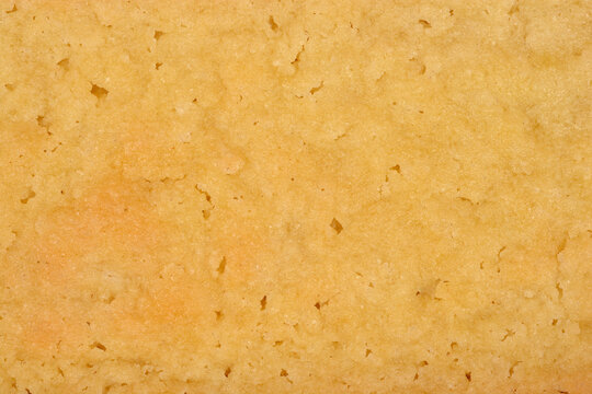 Macro background of a golden baked shortbread biscuit surface showing a crumbly porous texture made from butter flour and sugar.