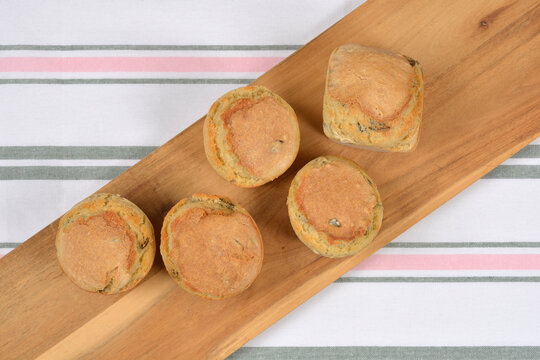 Top view of freshly baked small bread loaves with pumpkin seeds arranged on a wooden board over a striped tablecloth.