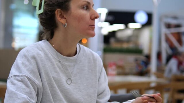 Casual woman enjoying a fresh vegetable salad with couscous and sauce for lunch, sitting at a wooden table in a bright, modern food court or restaurant, promoting a healthy lifestyle