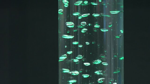 Close up footage of illuminated hydrogen bubbles rising inside transparent laboratory tube during clean energy experiment and electrolysis technology demonstration