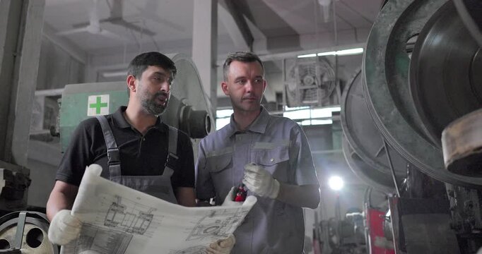 Factory Technicians Reviewing Blueprint During Machine Inspection in Metal Workshop