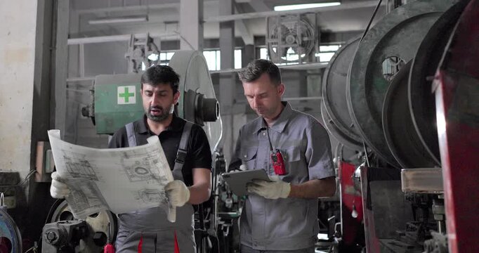 Factory Technicians Reviewing Blueprint During Machine Inspection in Metal Workshop