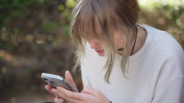 Close-up of focused teenage girl using smartphone in park, typing messages and scrolling on touchscreen outdoors. Modern youth, digital communication, and mobile lifestyle concept.