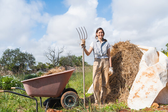 Woman smiling holding pitchfork on outdoor permaculture farm