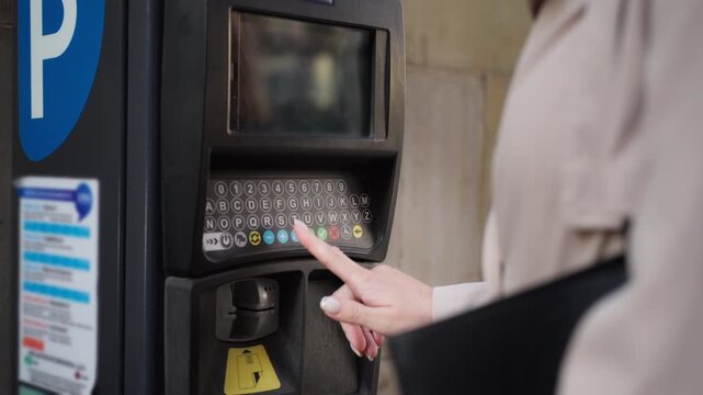 Close-up of female hand entering car license plate number on parking meter and paying with credit card. Modern cashless payment, urban mobility, and smart city parking system concept.