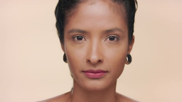 Big close-up shot of latin woman light brown complexion opens eyes for camera revealing moisturized skin on tan background | Beauty commercial concept