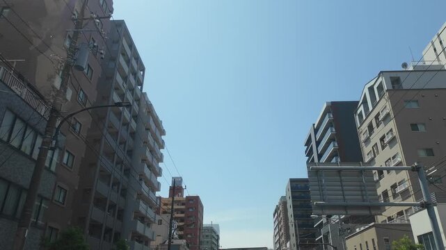 Hyperlapse driving view looking up at buildings, power lines, and clear blue sky in Tokyo, Japan (Japanese text on various signboards translates to "Pharmacy", convenience store names, and local busin