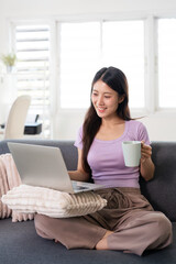Obraz premium Relaxing at home. young woman using laptop and smiling while drinking coffee or tea.