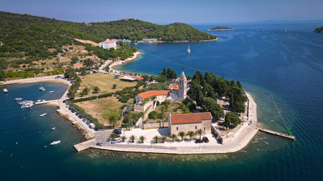 Aerial view of the Franciscan Monastery of St. Jerome on Prirovo peninsula with its stone bell tower and red roofs surrounded by turquoise sea in Vis, Split-Dalmatia County, Croatia.