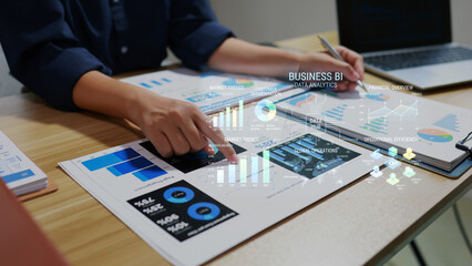 Fototapeta premium Business professional analyzing data charts and dashboard on desk with laptop, reports, and digital business intelligence analytics overlay in modern office.