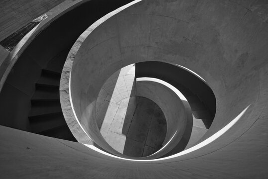 High-contrast black and white photograph of a spiraling concrete staircase highlighting geometric curves, light and shadow, minimal architectural form and abstract perspective.