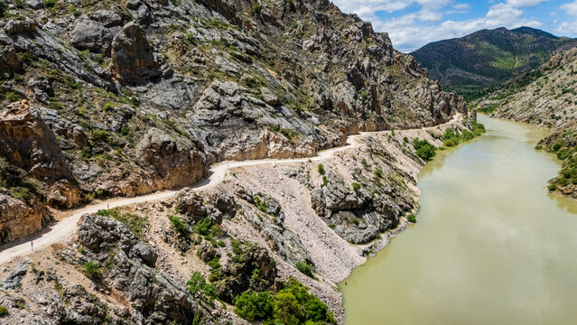 Aerial perspective flying through the deep Dark Canyon in Kemaliye, Turkey. Drone shot following the path of the Karasu River with the legendary hand-carved Stone Road visible on the cliff
