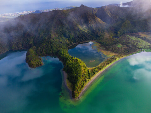 Aerial view of Lagoa do Fogo crater lake with turquoise water and lush green volcanic slopes under a misty sky in Agua de Alto, Azores, Portugal.