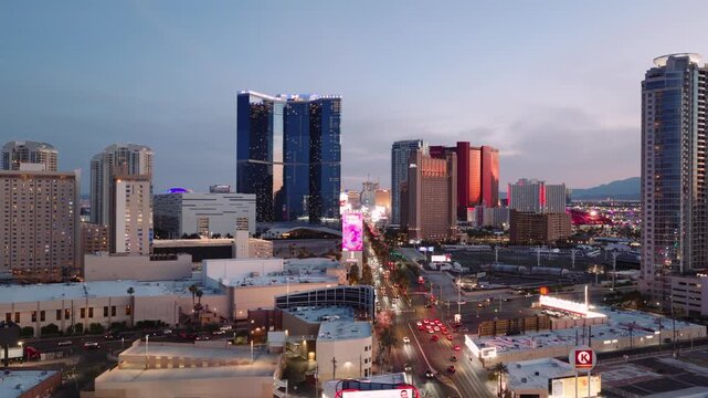 A cinematic aerial view of the Las Vegas Strip at sunset featuring the illuminated skyline, luxury resorts, observation wheel, and modern entertainment architecture. The vibrant cityscape captures the