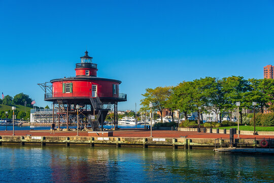 A bright daytime view of the historic red Seven Foot Knoll Lighthouse situated on a brick pier overlooking the water at the Inner Harbor in Baltimore, Maryland