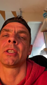 Indoor closeup white man vlogger talking, warm golden light, red hoodie and backward cap, home studio backdrop, direct eye contact, personal storytelling