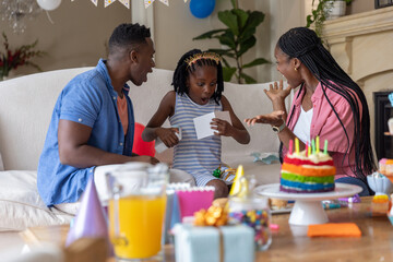 Fototapeta premium African American family celebrating at home, child in striped dress and gold headband holding card
