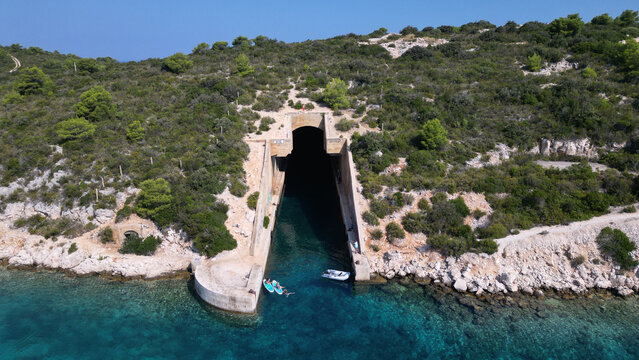 Aerial view of the Yugoslav army underground boat shelter Potkop Parja with people on paddleboards in turquoise water in Rogacic, Splitsko-dalmatinska, Croatia.