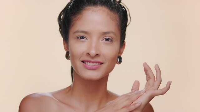 Close-up shot of argentinian woman with bronzed skin strokes forehead, touching her face with both hands focusing on balanced skin over tan background | Skin care ad