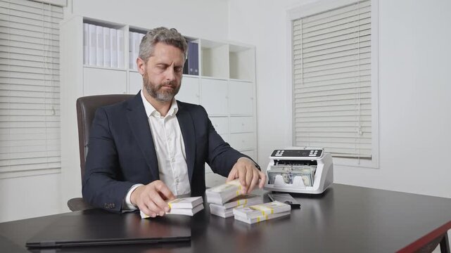 Businessman working on laptop with stacks of money in office. Business concept with cash and digital work. Banker in office. Banking operation in office with laptop and dollars. Business success theme