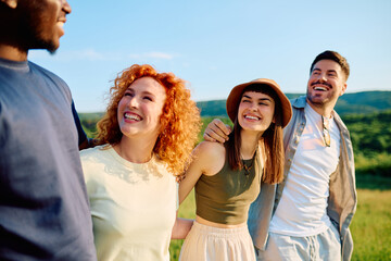 Group of happy diverse friends smiling and laughing together while walking outdoors through green fields on a sunny summer day