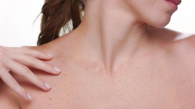 Closeup of Spanish woman with fair skin and freckles strokes her clavicles demonstrating hydrated skin on white background | Body care concept