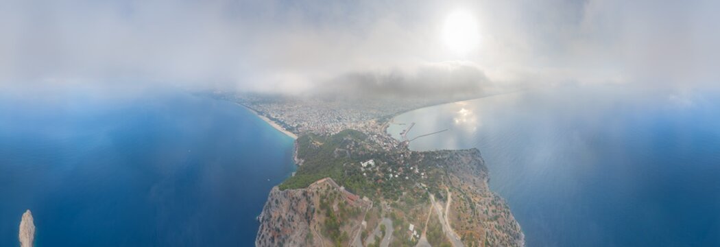 Alanya, Turkey. Cylindrical panoramic view from within the clouds overlooking Dil Varna Burnu, historic fortress, yacht marina and coastal plain in soft morning light. Panorama 360. Aerial view
