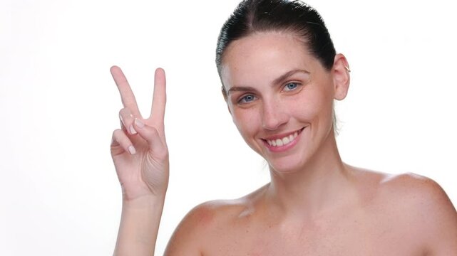 Close up of light-complexioned Latina with freckles with blue eyes and ponytale hairstyle showing a peace sign against white bg | Cosmetic product ads