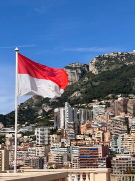 National flag of Monaco waving on a flagpole in Monte Carlo with trees and buildings in background