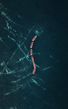 Aerial view of Lake Braies with a line of wooden rowing boats floating on the dark turquoise water surface in Braies, Trentino-Alto Adige, Italy.