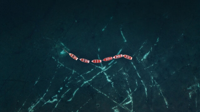 Aerial view of wooden rowing boats floating in a line on the turquoise water Braies, Trentino-Alto Adige, Italy.