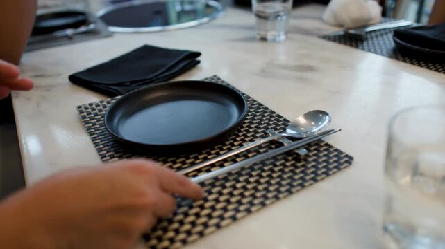 Person Arranging Silver Chopsticks and Spoon on Korean Restaurant Table