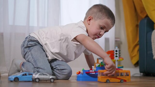 Student boy places car in toy lane. Student adjusts line with child control. Kid enjoys colorful parking setup. Boy imagines road system. Creative kid acts like student in smart learning moment.