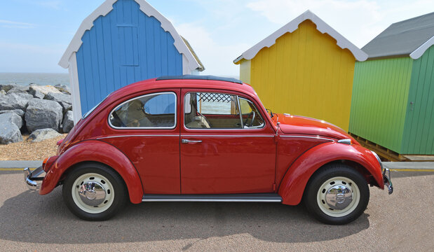 Classic Red Volkswagen Beetle parked in  front of beach huts on seafront promenade