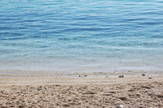 Scenic view of small waves lapping onto a smooth pebble beach with clear blue sea water.