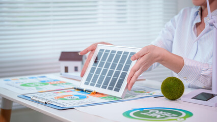 Consultant holding solar panel model over energy-efficiency charts and house model on office desk, renewable energy planning and green home concept. © Phushutter