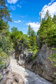 Water plunges down from Lech Falls into Lech Gorge. Surrounded by trees and rocky cliffs, this natural site shows the beauty of the area. Visitors enjoy the view on a sunny day.
