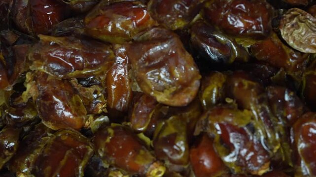 Close up of a hand reaching out and picking up a single fresh date fruit from a clean surface.