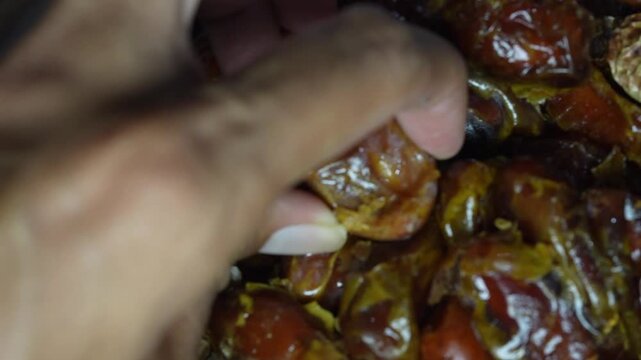 Close up of a hand reaching out and picking up a single fresh date fruit from a clean surface.