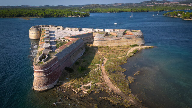 Aerial view of St. Nicholas' Fortress, a triangular stone fortification surrounded by the blue waters of the Adriatic Sea near green hills in Sibenik, Croatia.