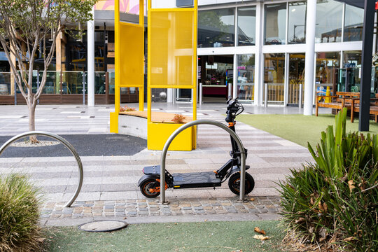 An electric kick scooter parked and locked to a bike rack outside a shopping mall entrance in Australia. This eco-friendly micro-mobility solution offers convenient urban transport for short commutes